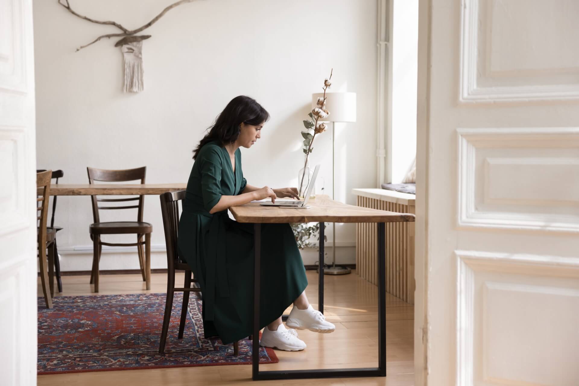 自然光の入る部屋で、一人でノートパソコンに向かって仕事をする女性
