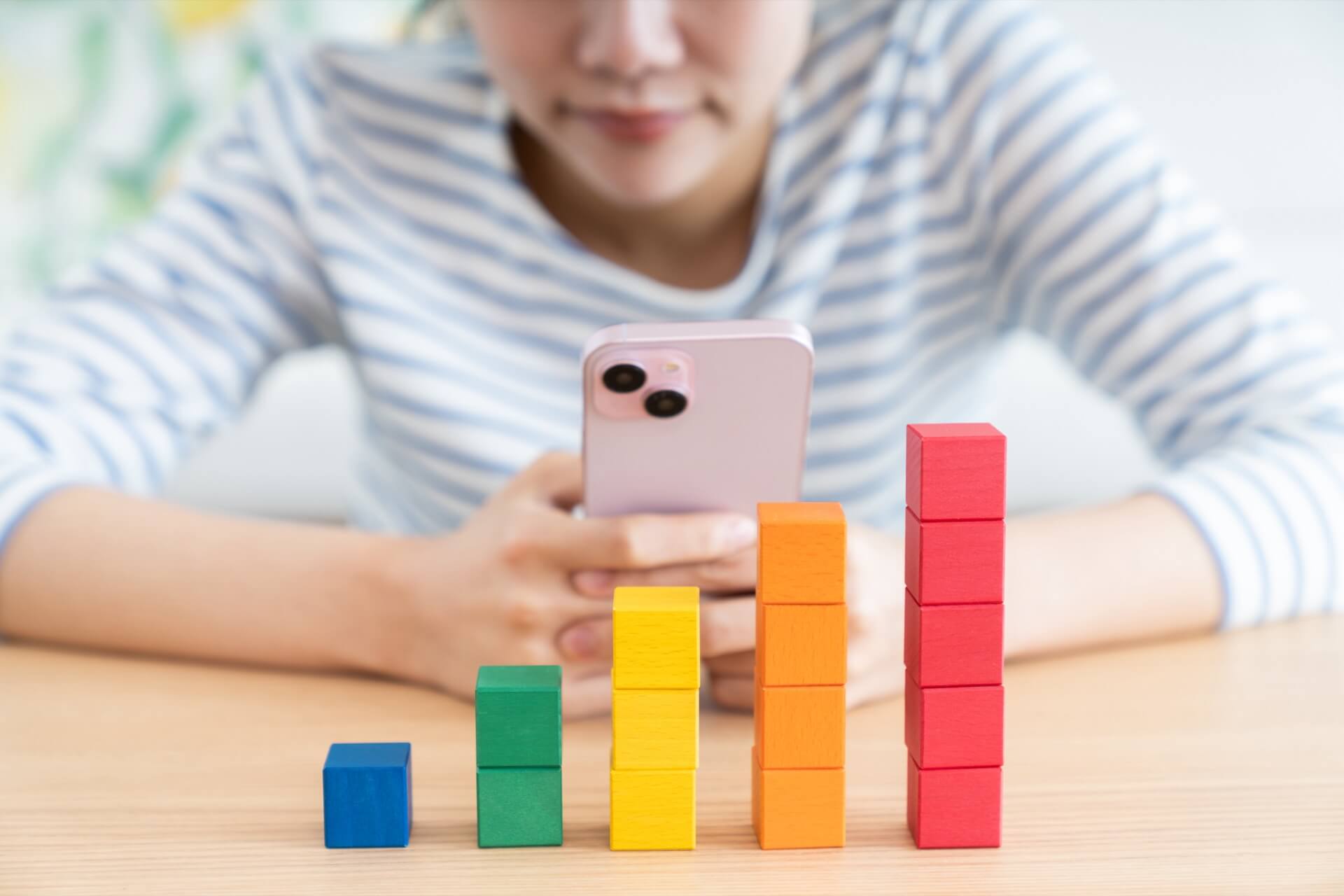 スマートフォンを手に持ち、色とりどりの積み木を階段状に積み上げて笑顔を見せる女性